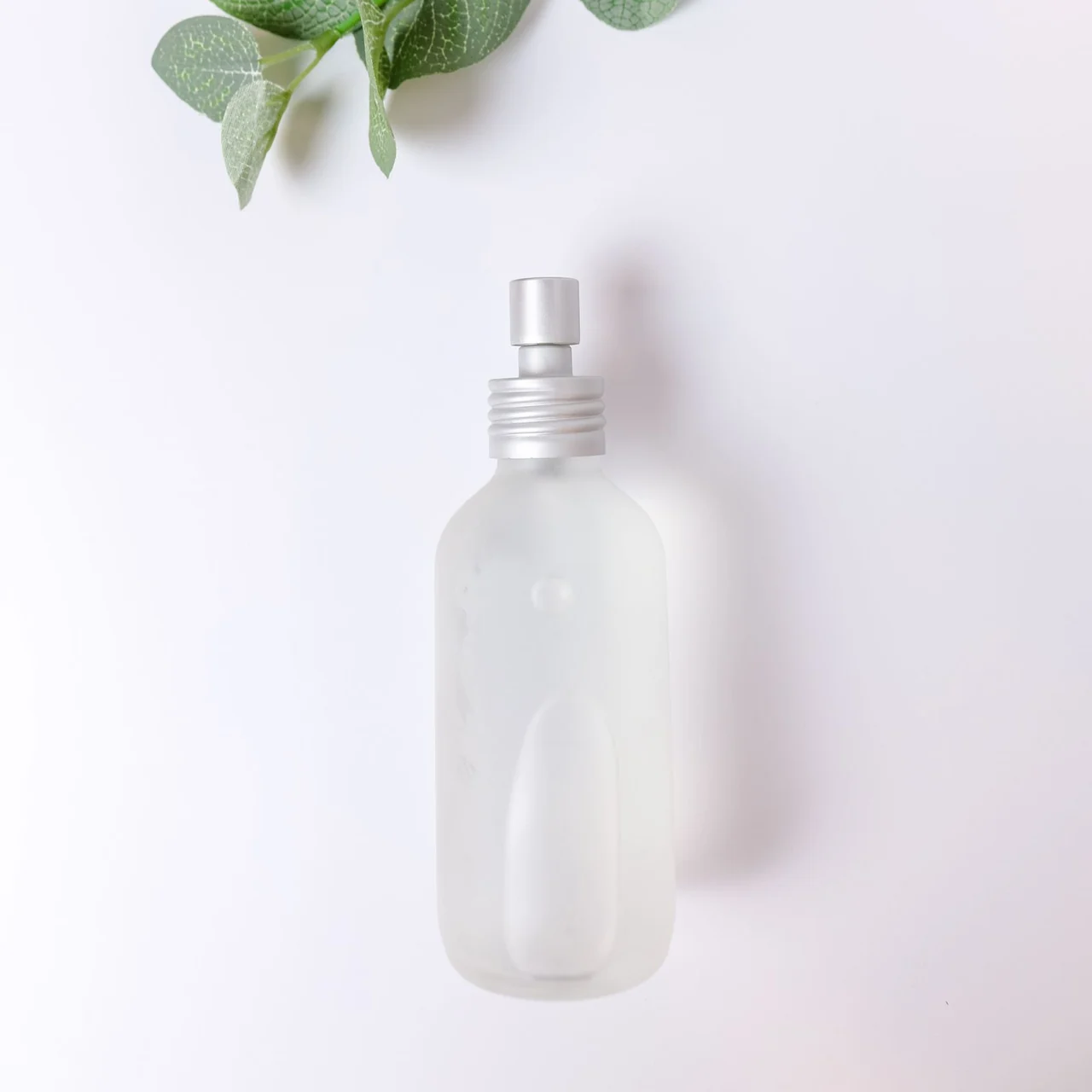 Real photograph of a frosted glass spray bottle illustrating body fragrance packaging
