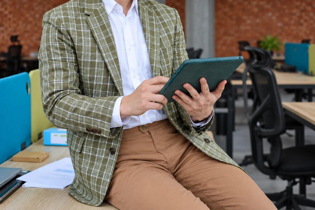 Hands holding a tablet beside a checked blazer in a shared office