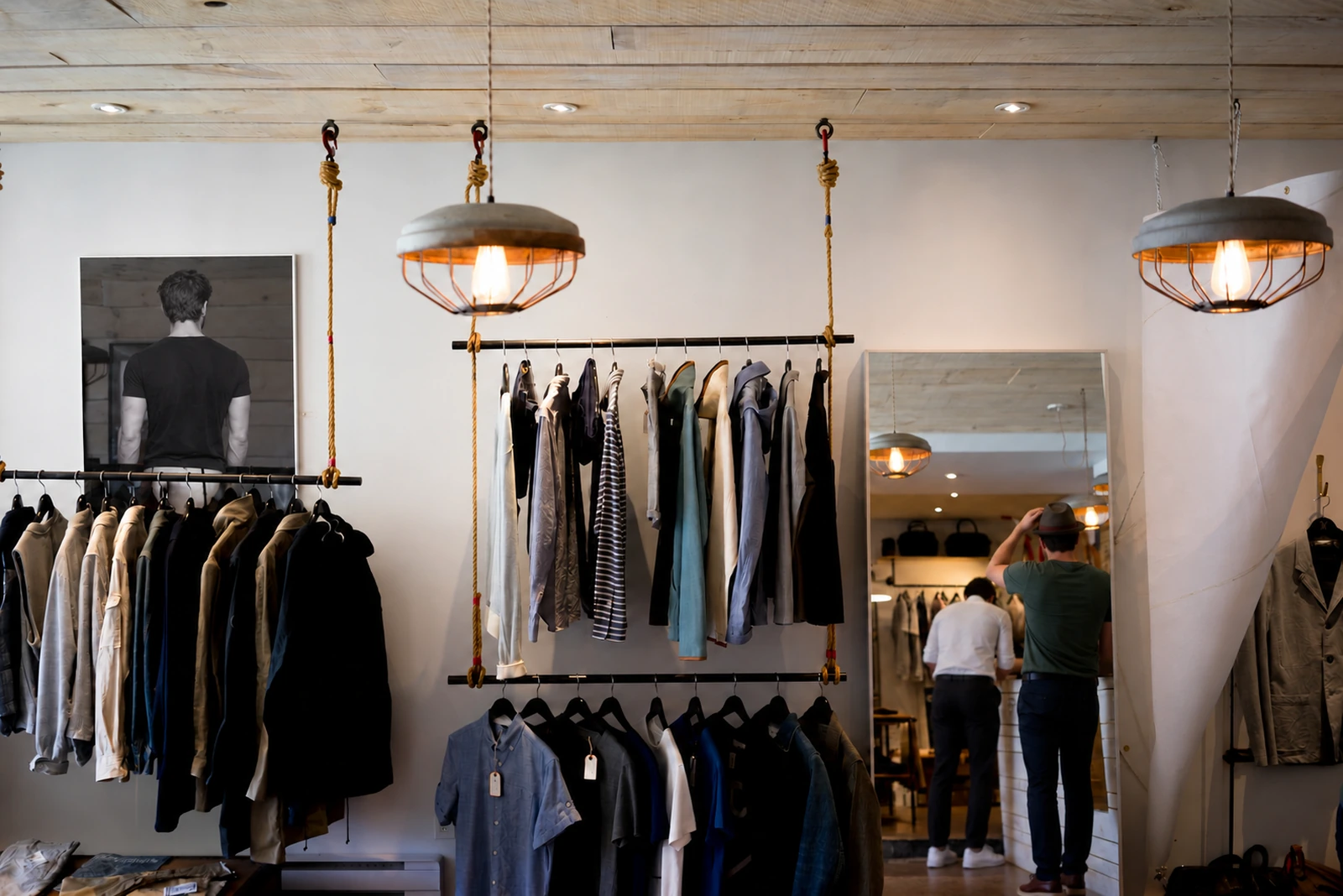 A small clothing boutique with wall mounted rails, warm lights and a mirror